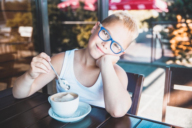 Красивый белокурый мальчик в белой футболке в ресторане, пьющий кофе
