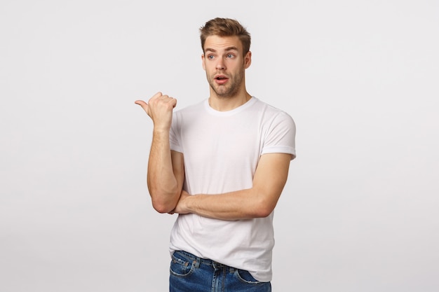 Handsome blond guy with blue eyes and white T-shirt pointing to the side