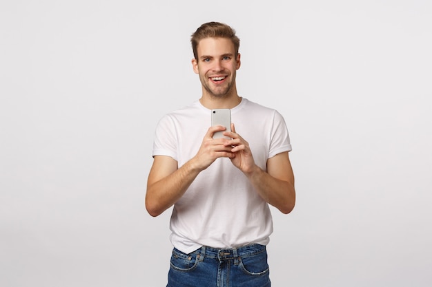 Ragazzo biondo bello con gli occhi azzurri e la maglietta bianca facendo uso dello smartphone