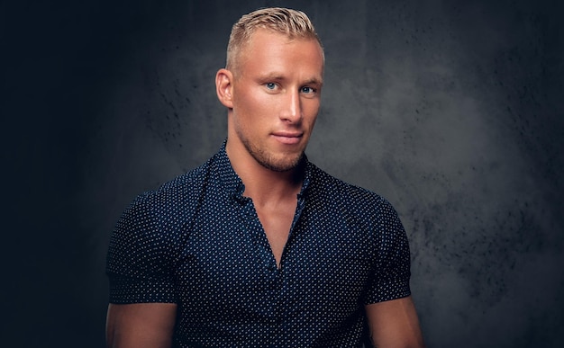 Handsome blond man in a dark blue shirt posing over grey background in a studio.