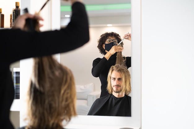 Handsome blonde male client getting haircut by black female hairdresser