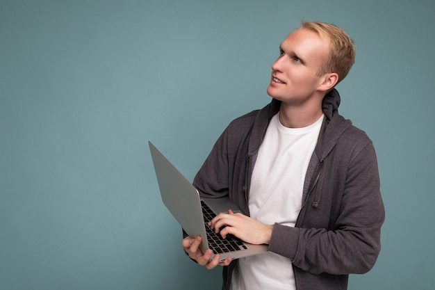 handsome blonde man holding computer laptop typing on keyboard thinking