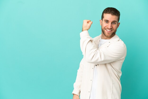 Handsome blonde man over isolated blue background doing strong gesture