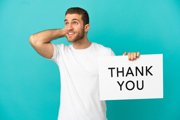 Handsome blonde man over isolated blue background holding a placard with text THANK YOU and thinking