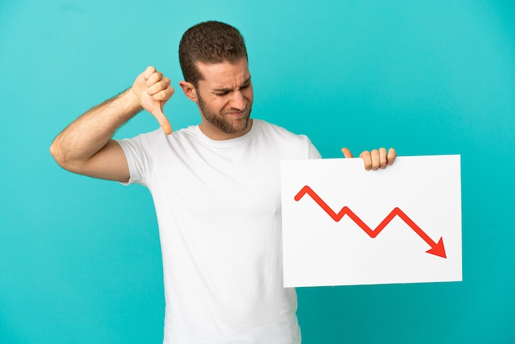 फोटो handsome blonde man over isolated blue background holding a sign with a decreasing statistics arrow symbol and doing bad signal