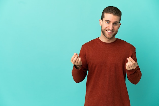 Handsome blonde man over isolated blue background making money gesture