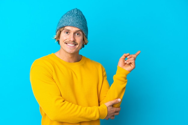 Handsome blonde man isolated on blue happy and pointing up