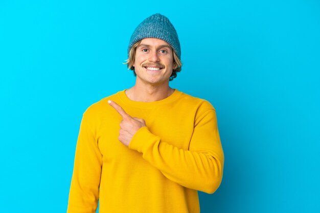 Handsome blonde man isolated on blue pointing to the side to present a product