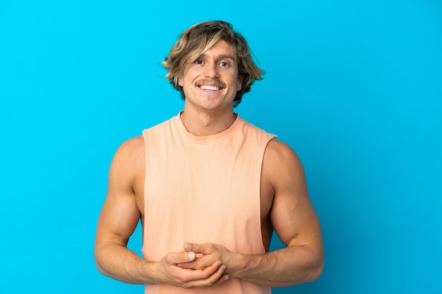 Handsome blonde man isolated on blue wall laughing