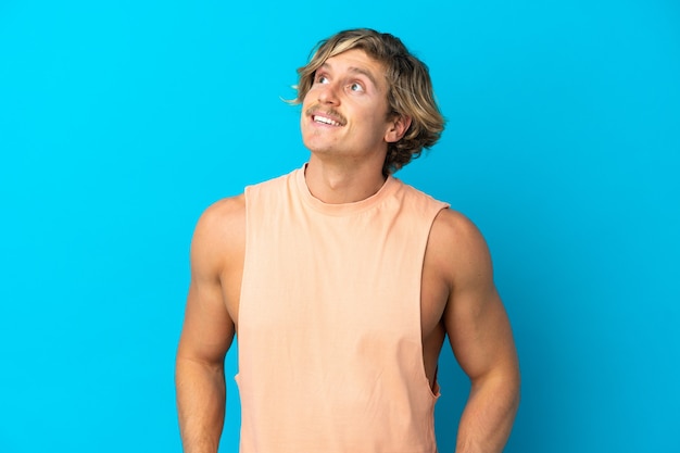 Handsome blonde man isolated on blue wall thinking an idea while looking up