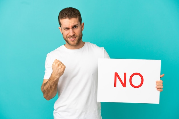 Photo handsome blonde man over isolated holding a placard with text no and angry