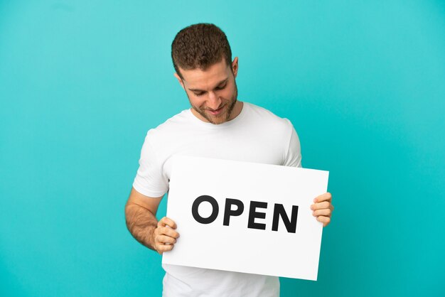 Handsome blonde man isolated holding a placard with text OPEN