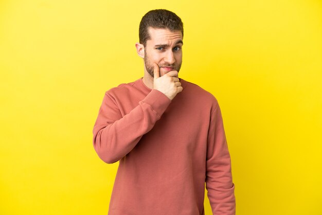 Handsome blonde man over isolated yellow background having doubts