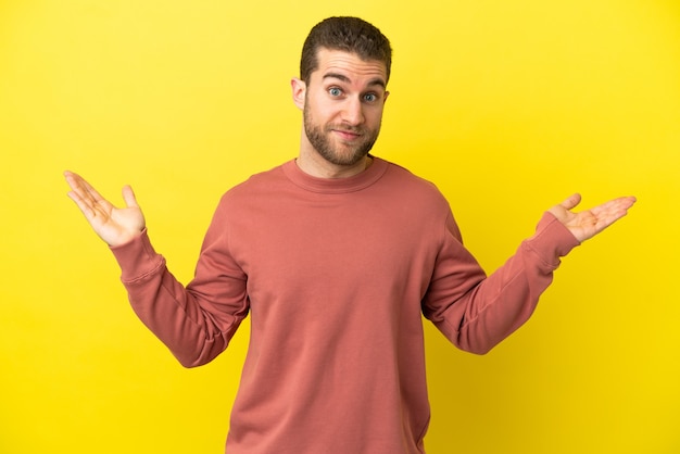 Handsome blonde man over isolated yellow background making doubts gesture