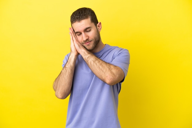 Handsome blonde man over isolated yellow background making sleep gesture in dorable expression