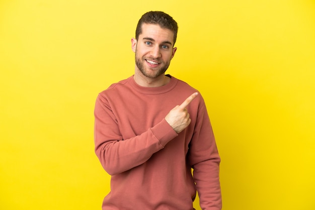 Handsome blonde man over isolated yellow background pointing to the side to present a product