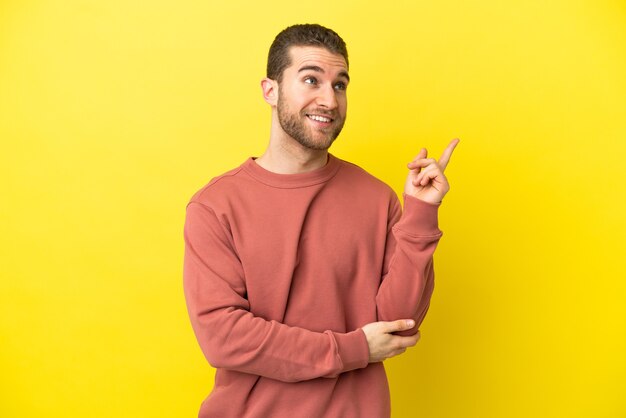 Handsome blonde man over isolated yellow background pointing up a great idea