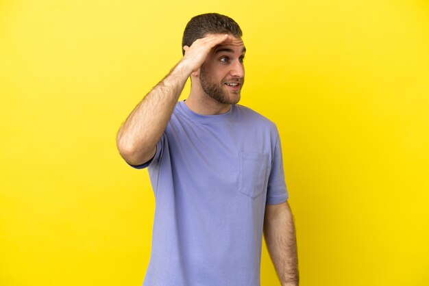 Handsome blonde man over isolated yellow background with surprise expression while looking side