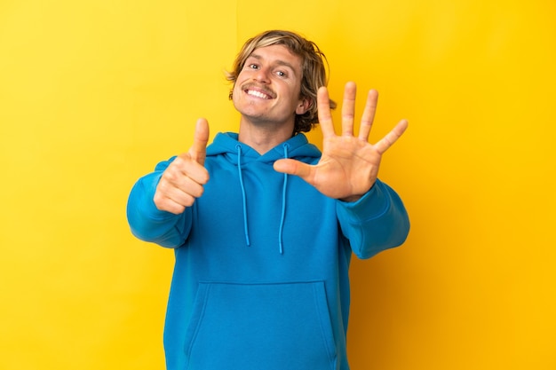 Handsome blonde man isolated on yellow counting six with fingers