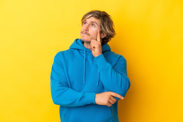 Handsome blonde man isolated on yellow wall having doubts and thinking