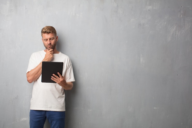 Photo handsome blonde man looking to a tablet pad over a grunge wall