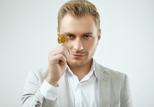 Handsome blonde man model in a fashion gray suit holds a Bitcoin