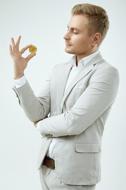 Handsome blonde man model in a fashion gray suit holds a Bitcoin