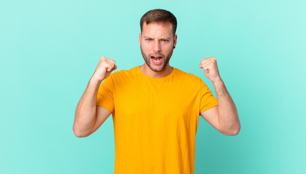 Handsome blonde man shouting aggressively with an angry expression