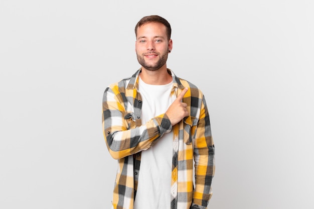 Handsome blonde man smiling cheerfully, feeling happy and pointing to the side