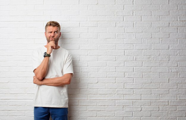 Handsome blonde man thinking against a grunge wall