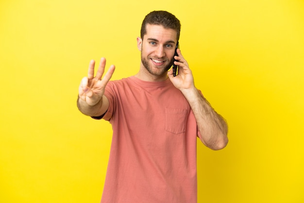 Красивый блондин с помощью мобильного телефона на изолированном фоне счастлив и считает три пальцами