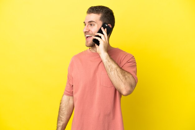 Handsome blonde man using mobile phone over isolated background laughing in lateral position