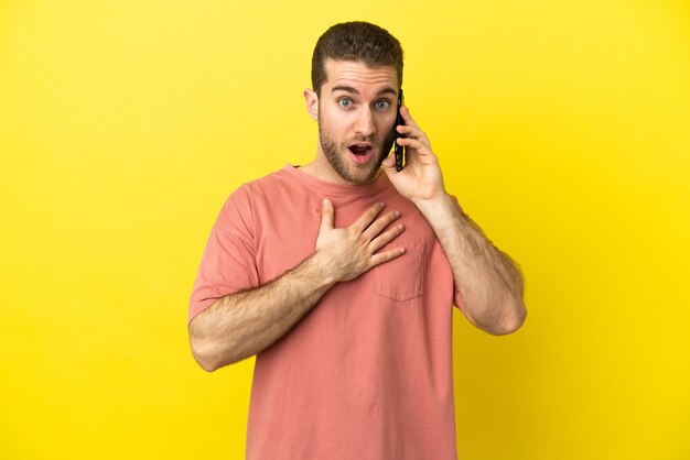 Bel uomo biondo utilizzando il telefono cellulare su sfondo isolato sorpreso e scioccato mentre guarda a destra