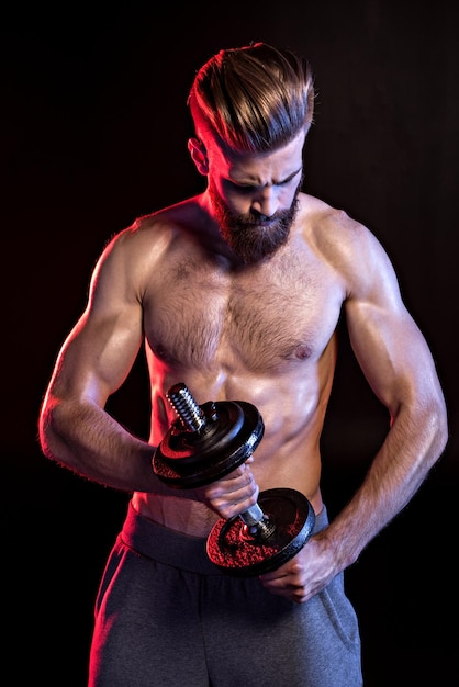 Handsome bodybuilder training with dumbbell isolated on black with dramatic lighting