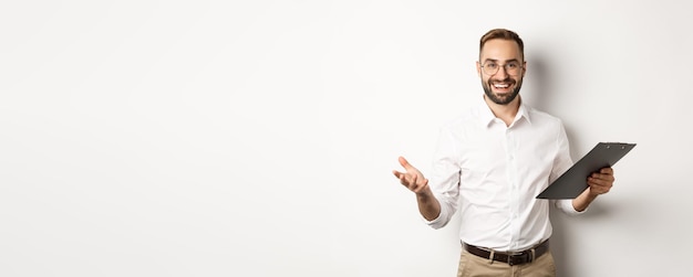 Photo handsome boss looking satisfied holding clipboard and praising you standing over white background