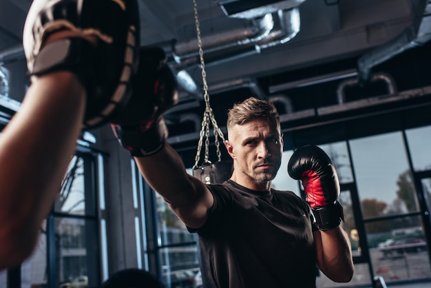 Handsome boxer exercising with trainer in gym