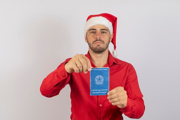 Handsome boy in Christmas clothes and Santa hat holding a Brazilian work card Concept of temporary jobs for the end of the year