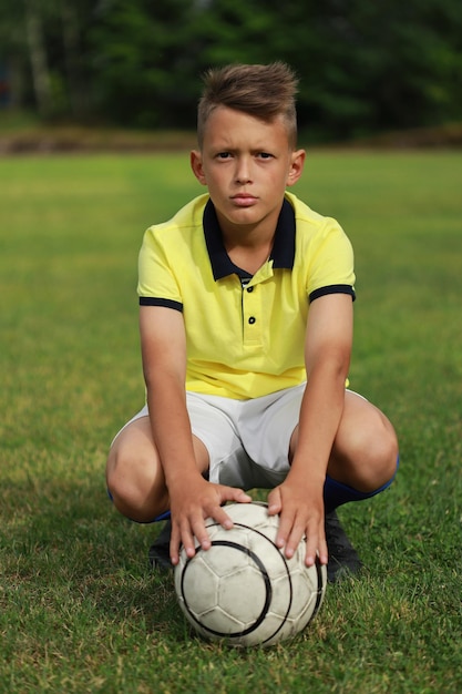 Красивый мальчик-футболист в желтой футболке сидит на футбольном поле