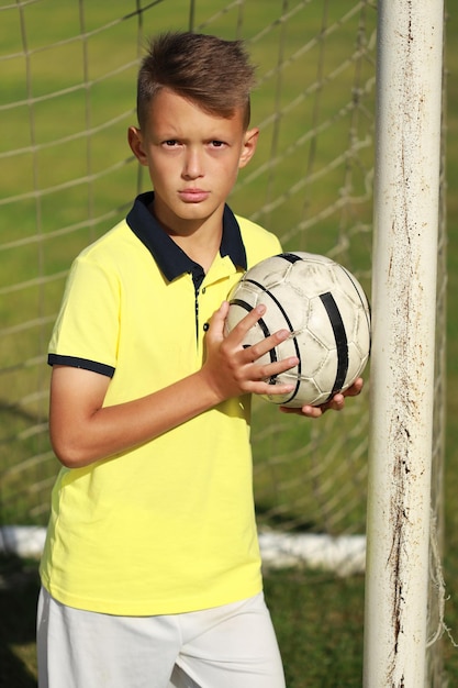Photo handsome boy football player in a yellow t-shirt stands near the goal with the ball
