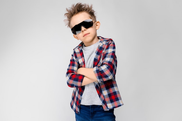 Foto un bel ragazzo in una camicia a quadri, camicia grigia e jeans si leva in piedi su gray