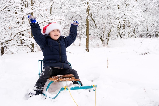 A handsome boy in a Santa Claus hat sits on a sled