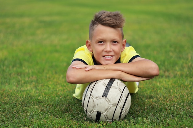 ハンサムな男の子のサッカー選手がボールを持ってサッカー場に横たわっている