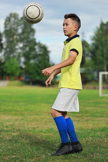 サッカー場の黄色いTシャツを着たハンサムな少年サッカー選手がボールをジャグリング