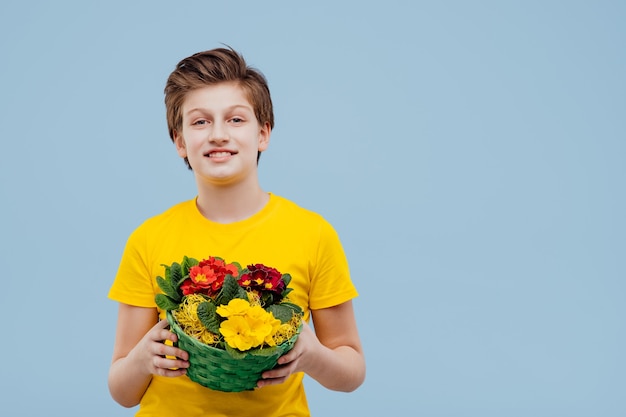 Photo handsome  boy with basket of flowers in his hand, in yellow t-shirt isolated on blue wall, copy space