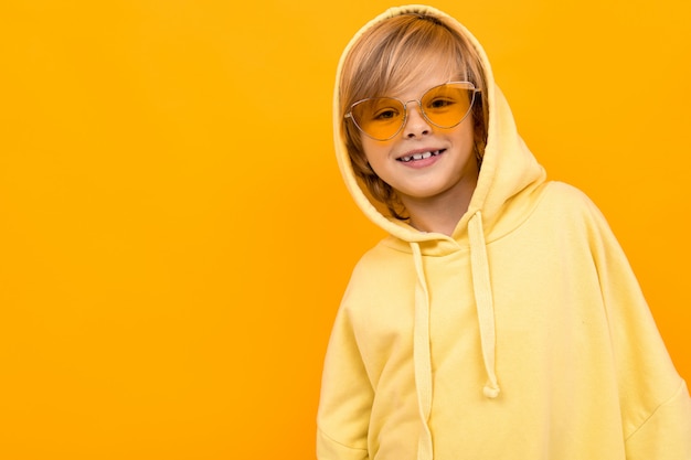 Handsome boy in yellow hoodie smiles and gesticulates isolated on orange