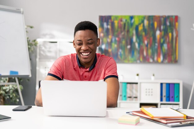 Handsome boy of young age sits at desk in front of laptop in\
room office next to him phone