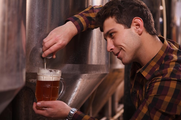 Foto bel birraio sorridente, versando birra artigianale in una tazza al suo microbirrificio