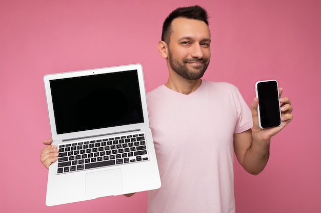 Handsome brunet man holding laptop computer and mobile phone fishily looking at camera