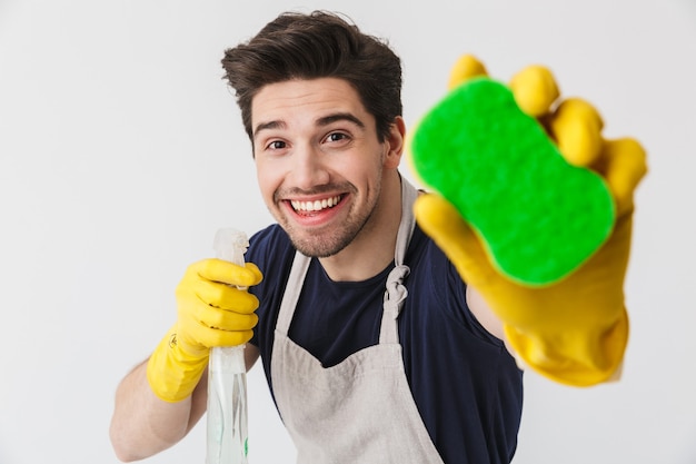 Handsome brunette houseman wearing apron standing isolated over white , holding sponges