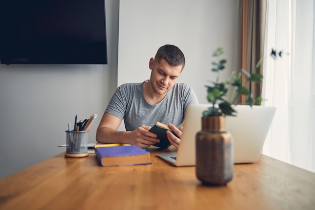 Handsome brunette male enjoying staying at home while spending time with book in living room